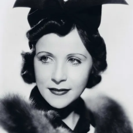  Black and white photograph of a woman wearing an extravagant black hat and a fur-trimmed top.