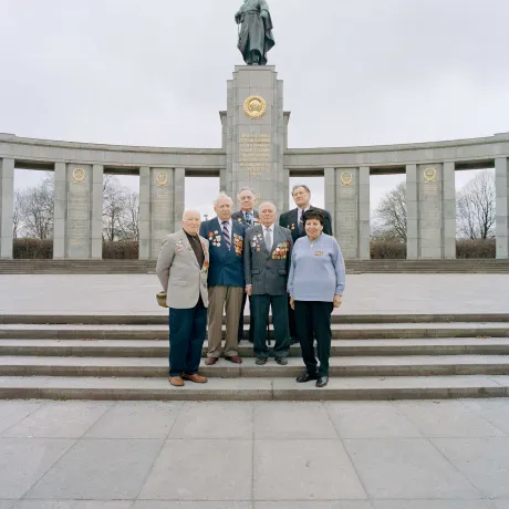 Alte Menschen stehen auf der Treppe vor einem Denkmal.