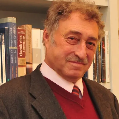 Ein Mann mittleren Alters steht vor einem Bücherregal und schaut in die Kamera