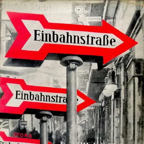Buchcover von Einbahnstra&szlig;e von Walter Benjamin: Schwarz-wei&szlig;-Fotografie einer Stra&szlig;e; im Vordergrund mehrere Verkehrsschilder mit rotem Pfeil und der Aufschrift &sbquo;Einbahnstra&szlig;e&lsquo;.