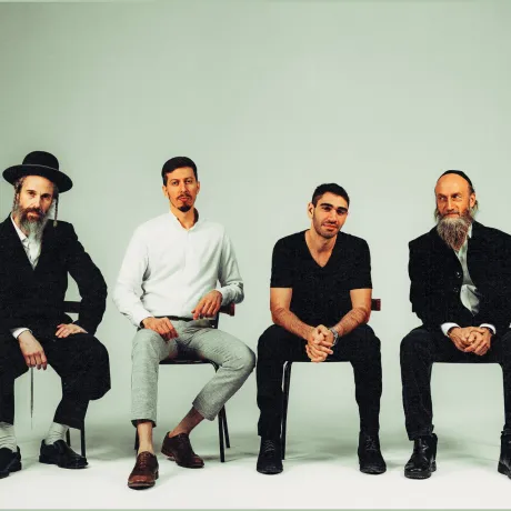 Four men are sitting in a row on chairs, casually looking at the camera.