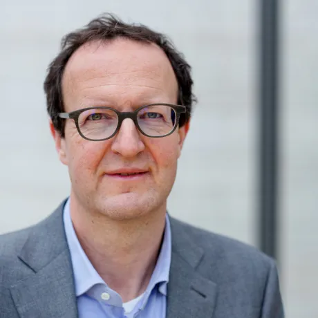 Mann mit Brille schaut freundlich in die Kamera und hat einen Anzug an.