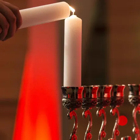 Eine Hand zündet mit einer Kerze die erste Kerze in einem Chanukka-Leuchter an.
