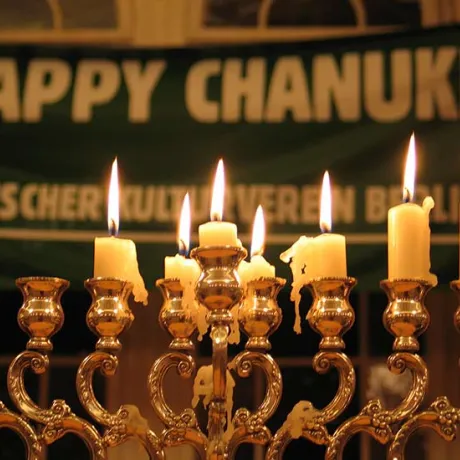 Hanukkah candlestick with burning candles, behind it a banner with the inscription: Happy Hanukkah. Jewish Cultural Association Berlin.