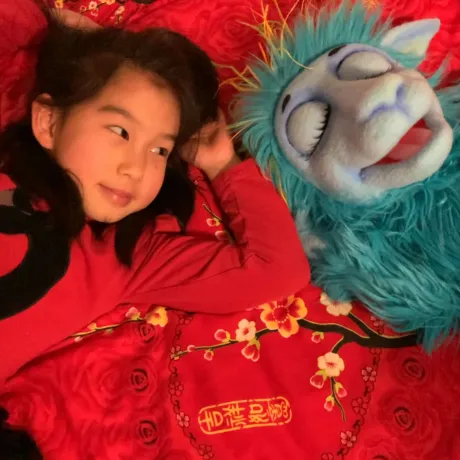 M&auml;dchen liegt mit dem j&uuml;dischen Fantasiewesen Gl&uuml;ckel auf einer roten Decke