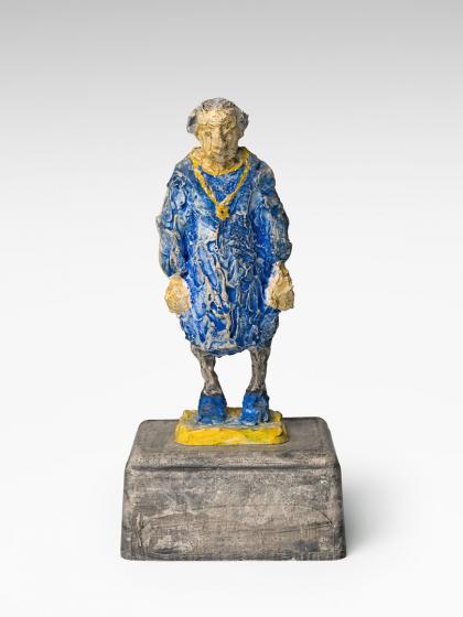 A figure with blue clothes stands on a pedestal.