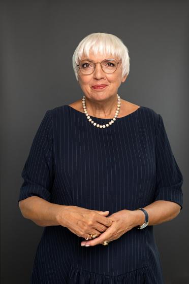 Portrait of Claudia Roth in black dress with white chain. She looks friendly into the camera.
