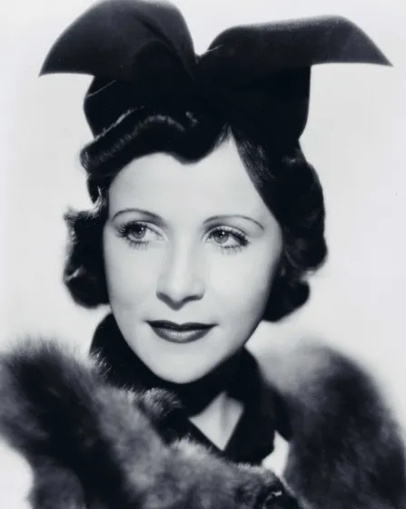  Black and white photograph of a woman wearing an extravagant black hat and a fur-trimmed top.