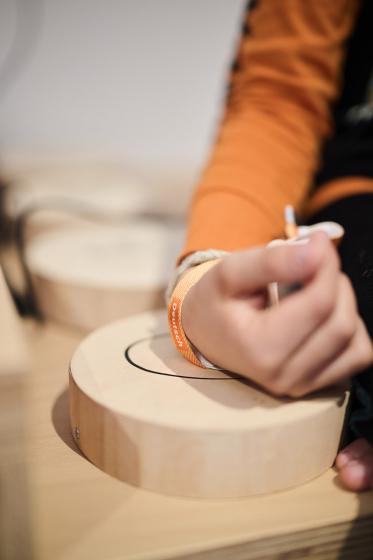 Child hand with orange bracelet touches a wooden box.