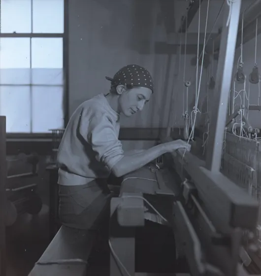 A woman sitting at and working on her loom. 