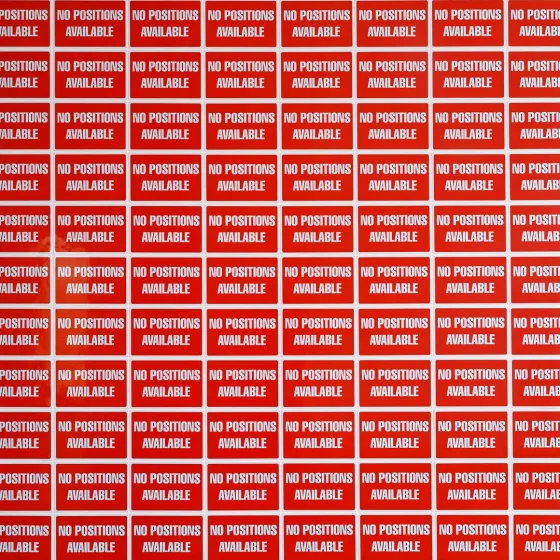 Eine Wand tapeziert mit rechteckigen, roten Schildern, auf denen steht: „NO POSITIONS AVAILABLE“.