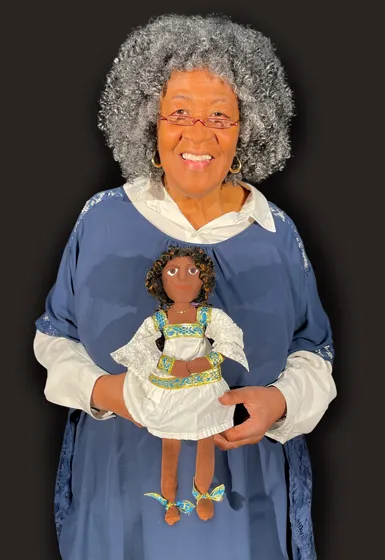 A woman with abundant grey hair is holding a puppet in her hands.