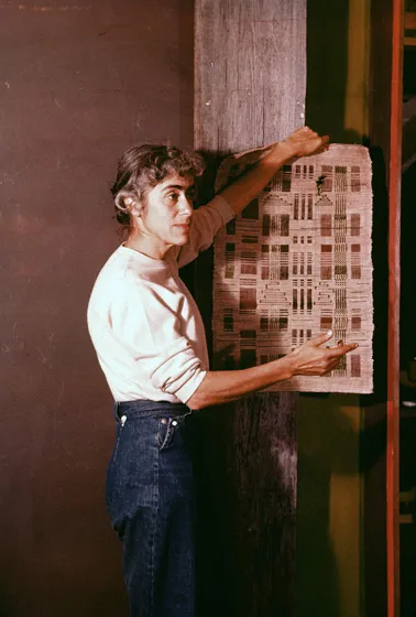  A woman in a white sweater and jeans stands against a wall.