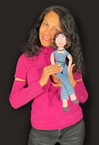 A woman with long dark hair is wearing a pink sweater and is holding a doll in her hands.