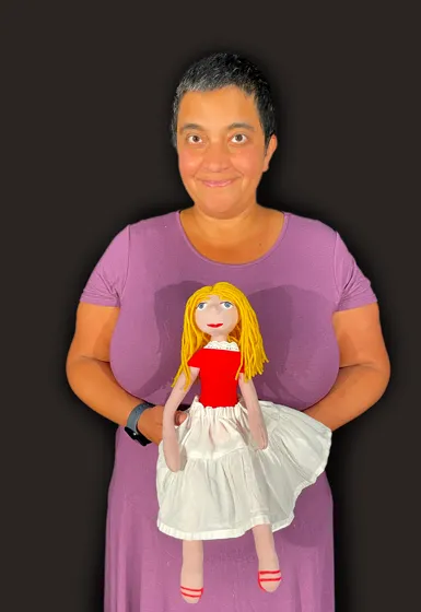 A woman with short dark hair, wearing a violet dress, is holding a doll in her hand.
