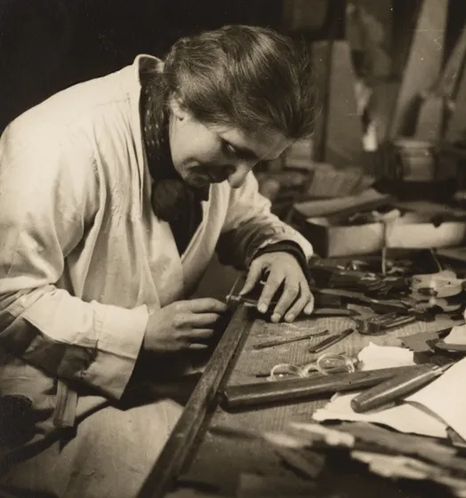 Historical photograph of a woman leaning forward at a workbench.