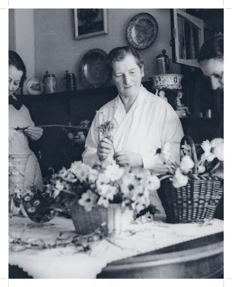 Sepiafarbene Aufnahme, die drei Frauen zeigt, die Blumengestecke in Weidenkörben zusammenstellen. 