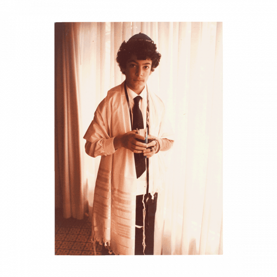 Portrait of Rabin Yaghoubi wearing a tallit, tefillin as well as a kippah. In his hands he holds a prayer book.