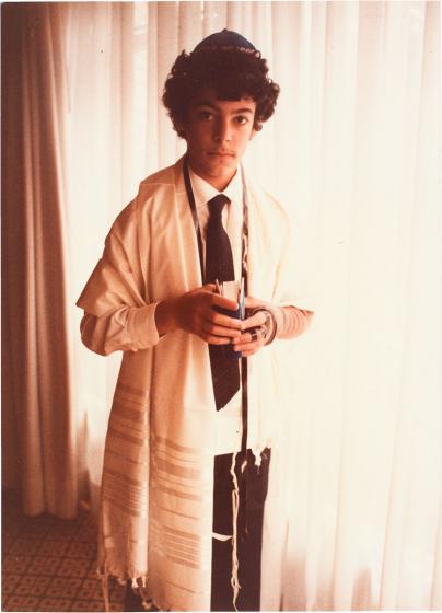 Porträt von Rabin Yaghoubi, der einen Tallit, Tefillin sowie eine Kippa trägt. In seinen Händen hält er ein Gebetbuch.