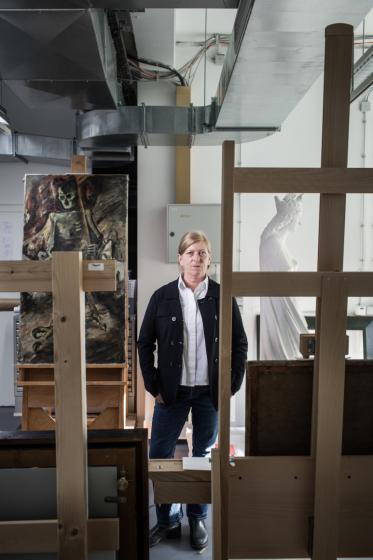 Eine Frau, stehend zwischen Staffeleien, Gemälden und Skulpturen in einem Atelier.