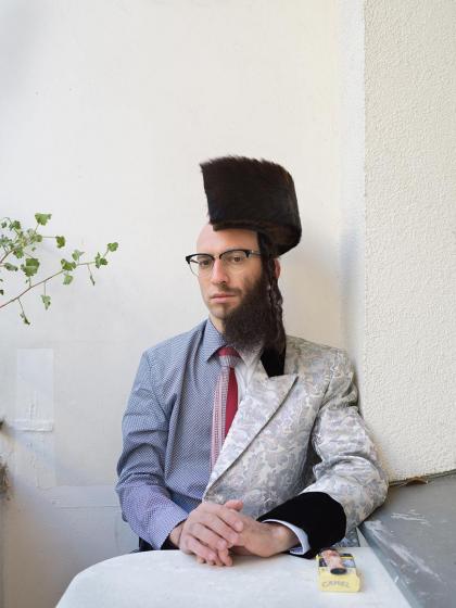 Photograph of a man divided along the longitudinal axis, as it were, into two halves: on the left side he wears a shirt and bald head, on the right a full beard and a (halved) shtreimel on his head 