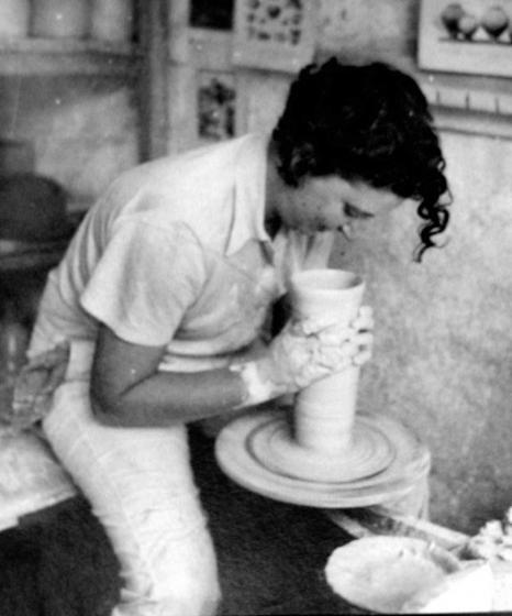 Black and white photo of Hanna Charag-Zuntz and the pottery wheel with her hands covered in clay