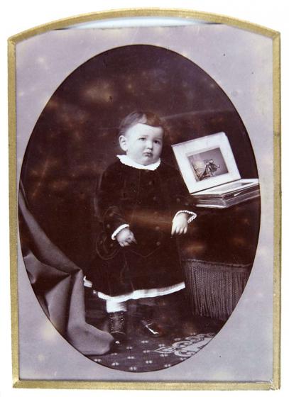 Black-and-white photo of a standing baby alongside an open photo album