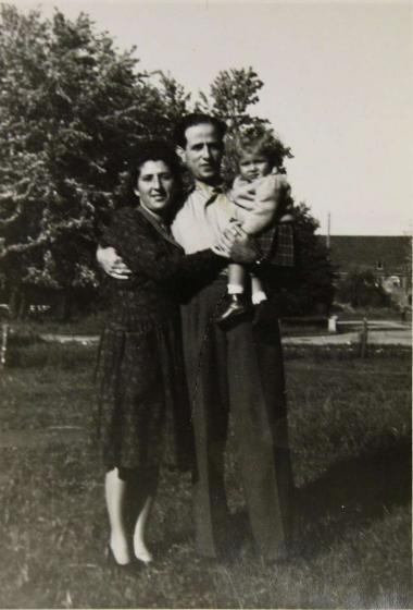 Schwarz-weiße Außenaufnahme einer Familie, der Vater trägt die einjährige Tochter auf dem Arm