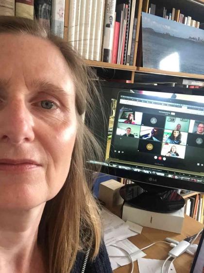 Selfie by Henriette Kolb, standing with her back to her screen on which a video call is open.