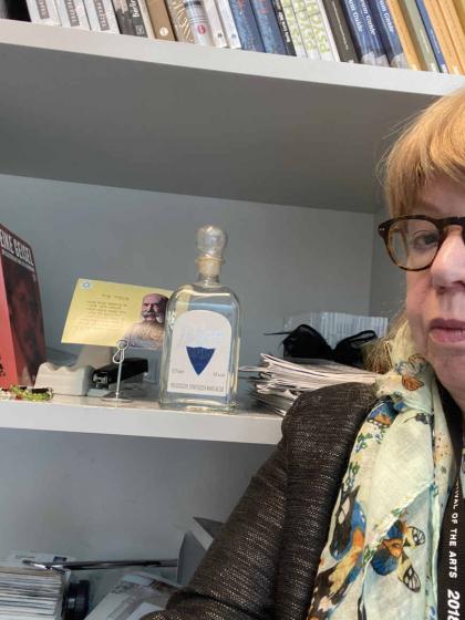 Selfie Cilly Kugelmann in front of a shelf with a vodka bottle and a postcard.