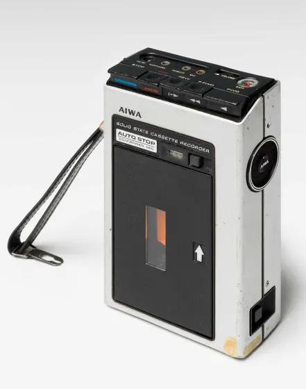 Fotografie eines Audioaufnahmeger&auml;ts f&uuml;r Tonkassetten mit schwarzer Lederschlaufe der Marke AIWA aus den 1970er Jahren. 