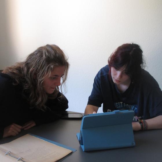 Two high school students conducting research with archival materials and a tablet