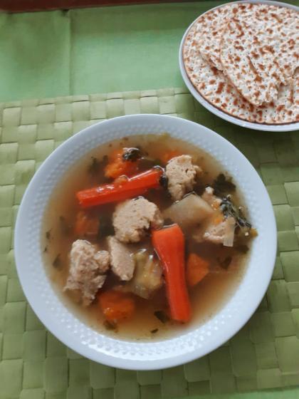 A plate of chicken soup, carrots and matzah balls stands on a green background. On another plate lies bread.