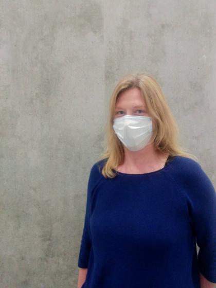 Portrait of Iris Saeger with breathing mask in front of concrete wall