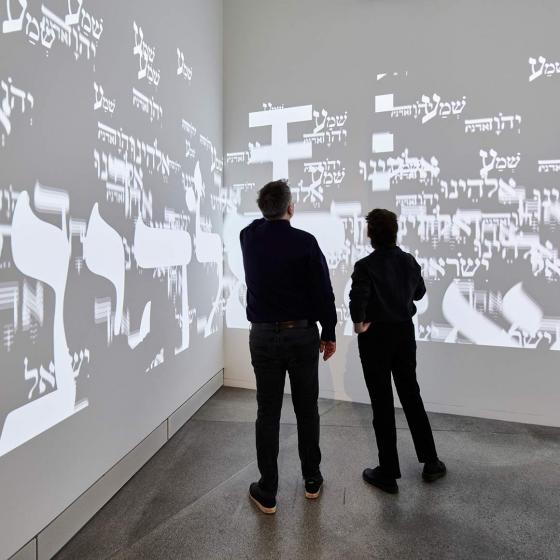 People watching a video projection of Hebrew letters on the walls of a room