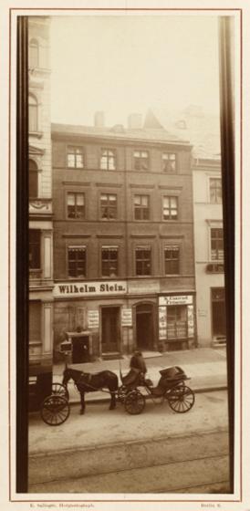 Vergilbtes Schwarz-Weiß-Foto eines Wohnhauses mit Pferdewagen vor der Tür und einem Schild über der Tür mit der Aufschrift: Wilhelm Stein.