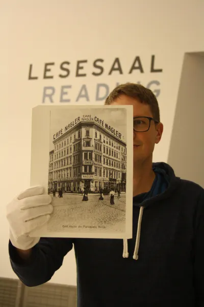 Ein Mann hält eine Schwarz-Weiß Fotografie vor sich. Auf dem Foto ist ein Gebäude abgebildet.