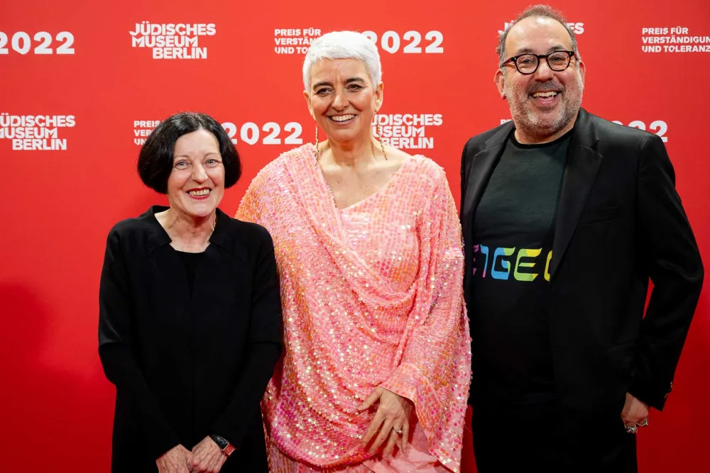 Hetty Berg in a red sequined dress between Herta Müller and Barrie Kosky, both in black, all laughing into the camera.