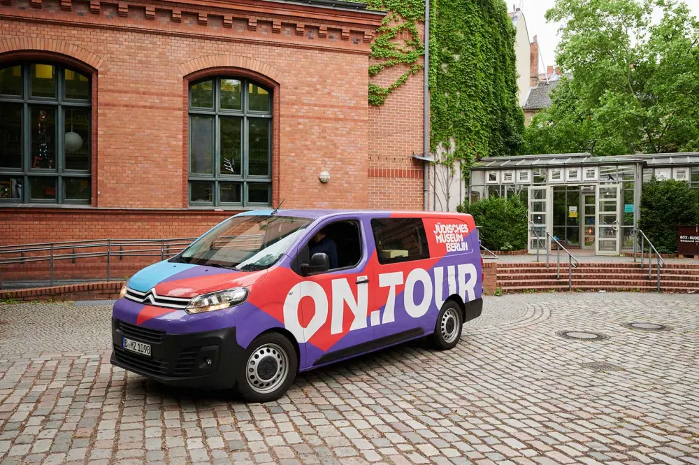 Red and purple van with the logo on.tour parked in a school yard.