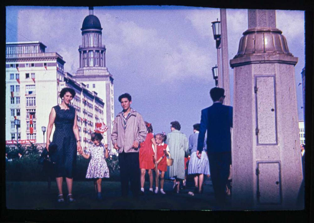 Foto von einer Frau mit Kind an der Hand, daneben ein Jugendlicher mit den sogenannten Arbeiterpalästen in der Stalinallee im Hintergrund.