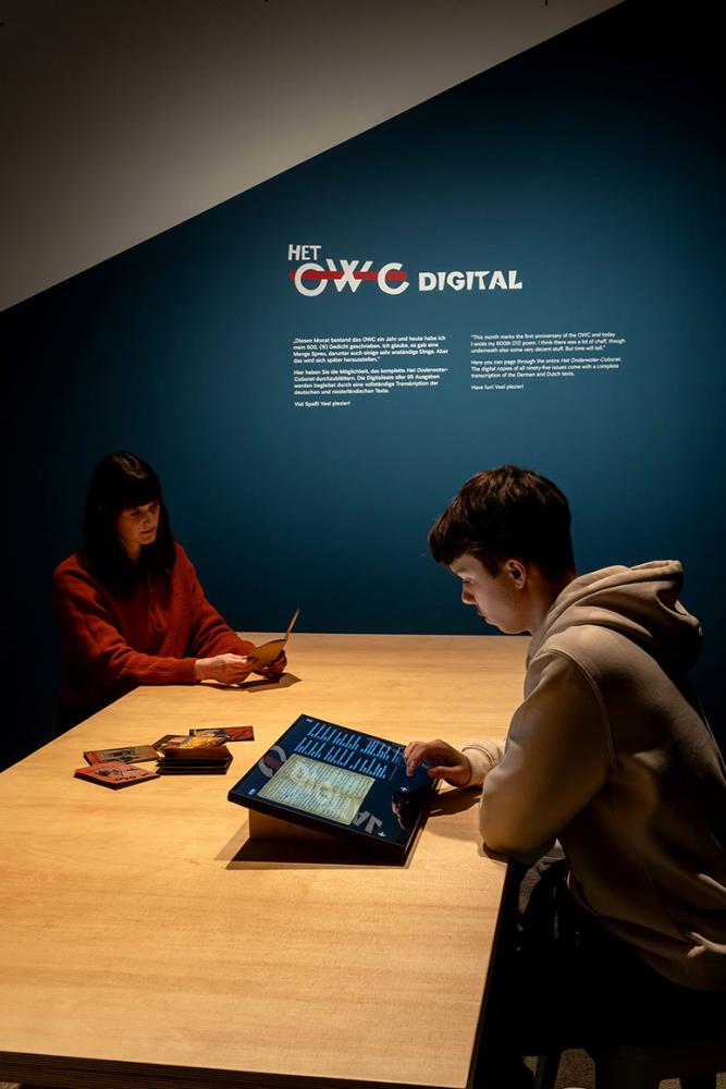 Raumansicht der Ausstellung "Het Onderwater Cabaret": zwei Besucher*innen schauen sich eine digitale Anwendung an.
