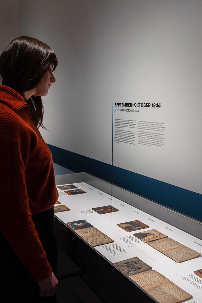 Raumansicht der Ausstellung "Het Onderwater Cabaret": eine Besucherin schaut sich Dokumente in einer Vitrine an.