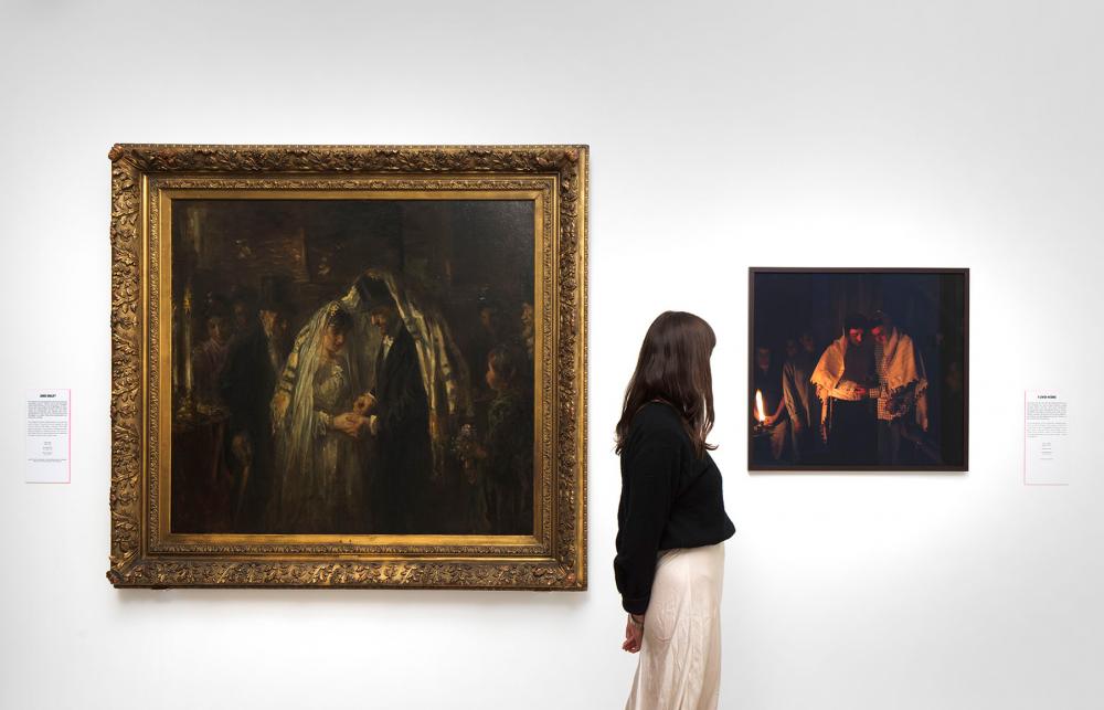 Ausstellungsansicht, eine Frau steht vor einer Wand an der links ein Gemälde und rechts eine Fotografie hängen.