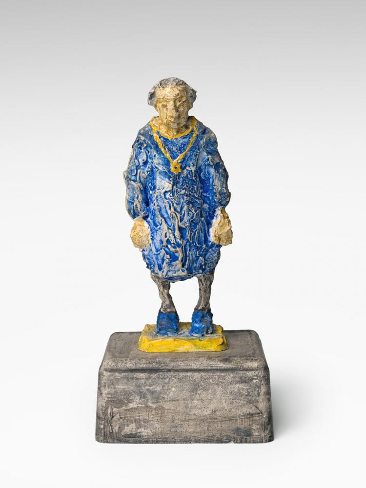 A figure with blue clothes stands on a pedestal.