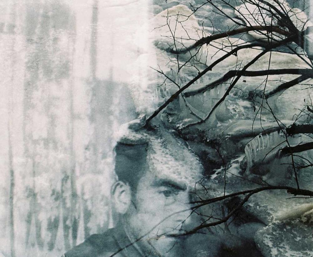 Schwarz-weiß Fotografie, im Zentrum ein Mann, um ihn herum Äste und ein gefrorener Wasserfall.