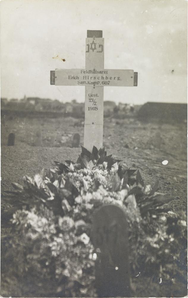 Schwarz-weiß-Foto: Blumengeschmücktes Grab mit Grabkreuz (Inschrift auf Deutsch und Hebräisch, Davidstern)