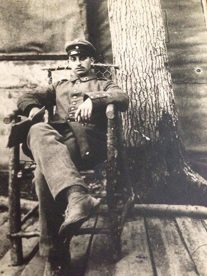 Black-and-white photograph: Soldier in uniform sitting in a chair with a tree trunk in the background