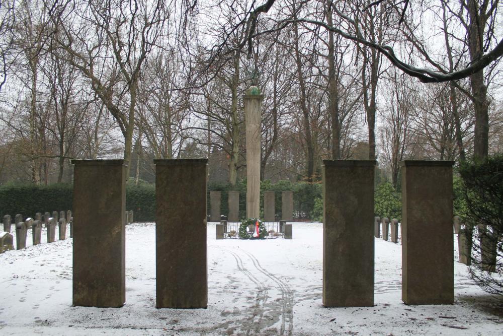 Farbfoto: Im Vordergrund vier Gedenksteine, im Hintergrund Obelisk mit bronzenem Lorbeerkranz gekrönt