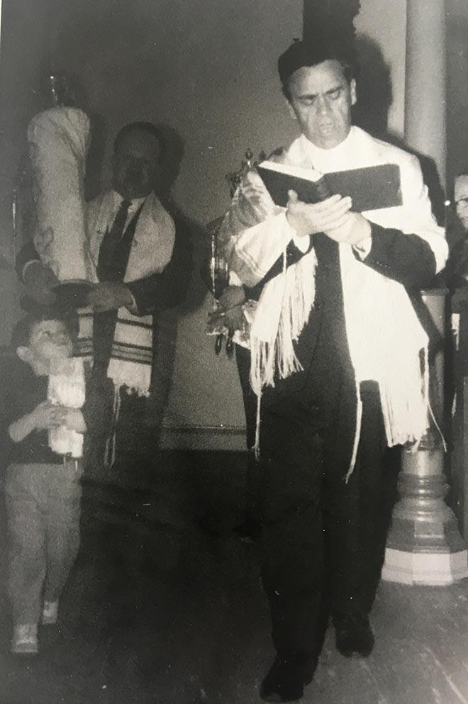 Schwarz-weiß-Foto eines stehenden Mannes mit Tallit und aufgeschlagenem Buch in den Händen