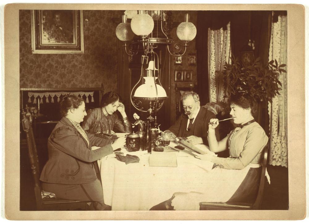 Four people at the living room table in a photograph around 1900.